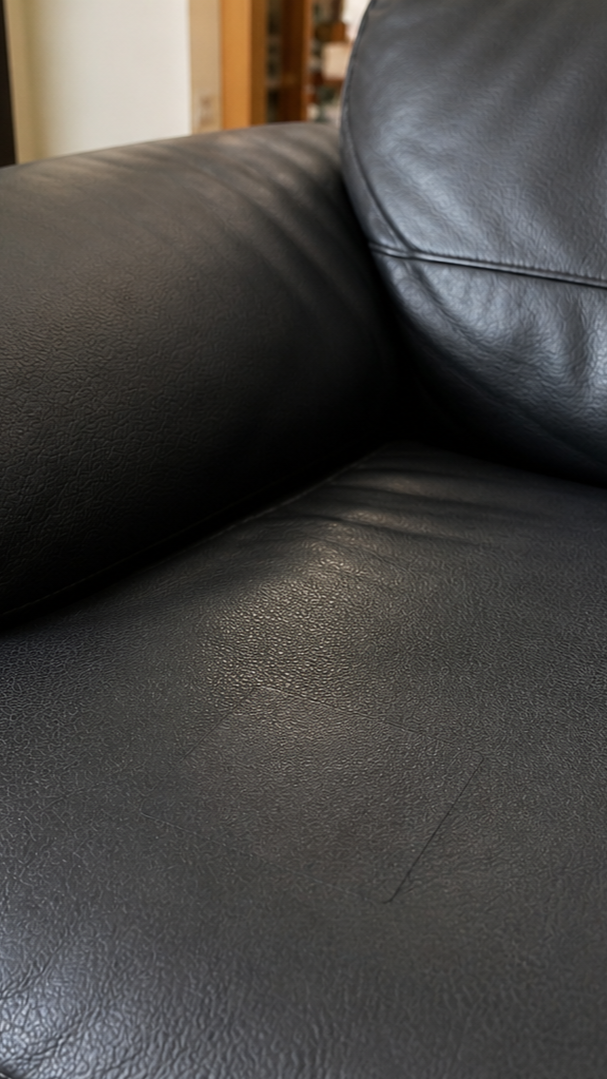 Close-up of a black leather couch with visible wear.
